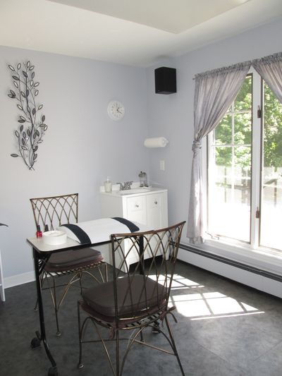 Two rod-iron chairs with manicure table. Sunshine flowing in window with green trees outside