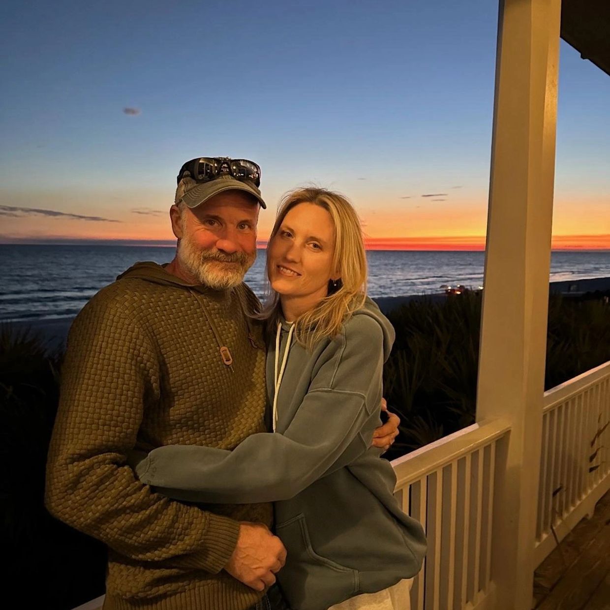 Couple hugging on a balcony with ocean sunset.