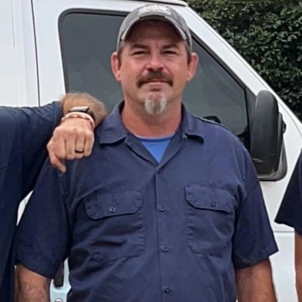 Man in work uniform and cap standing outdoors.