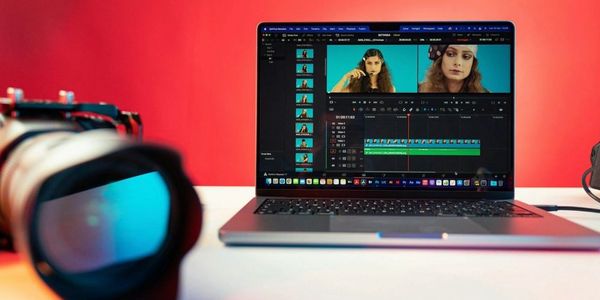 Laptop displaying video editing software with a camera lens in the foreground.