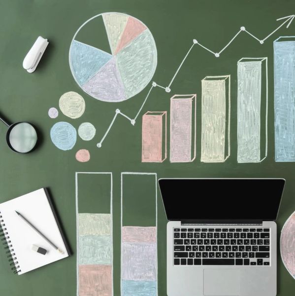 Office desk with laptop, coffee, and colorful chalk-drawn charts on a green board.
