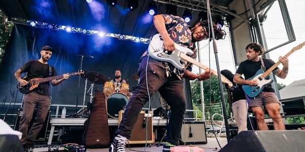 A lively outdoor band performance with five musicians playing guitars and drums.