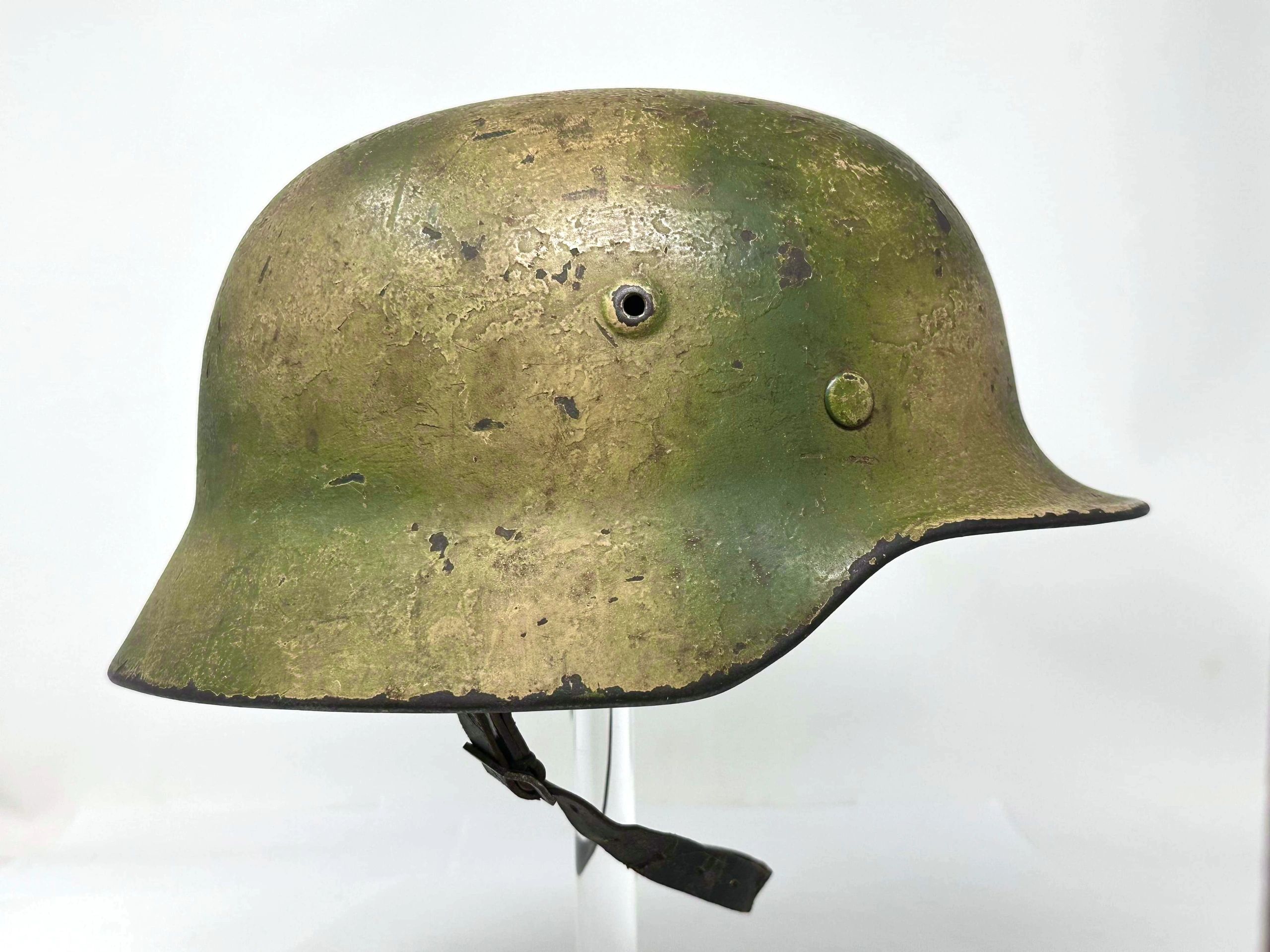Worn, green military helmet with scratches and leather strap.