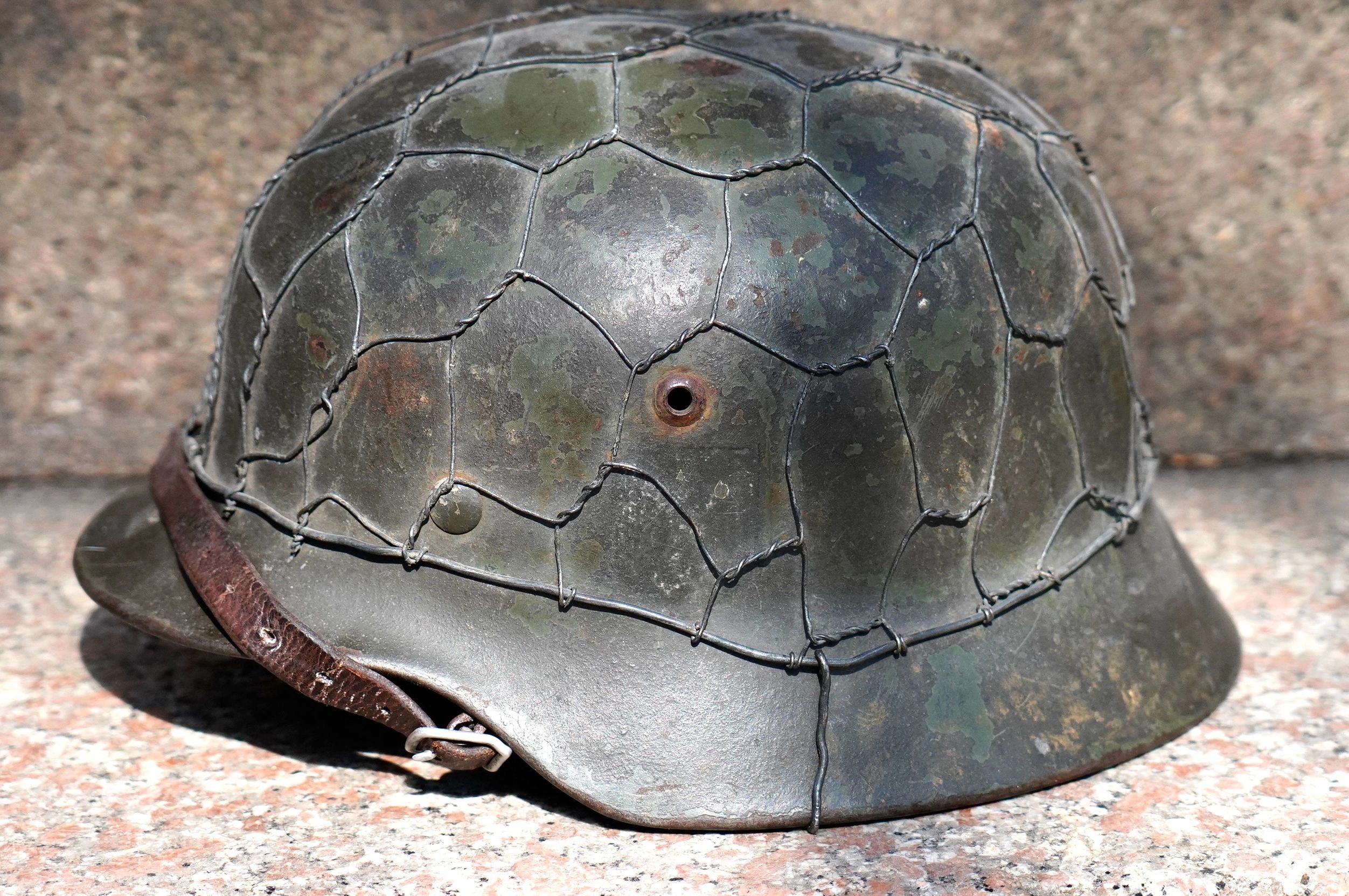 Close-up of a worn military helmet with wire mesh and leather strap.