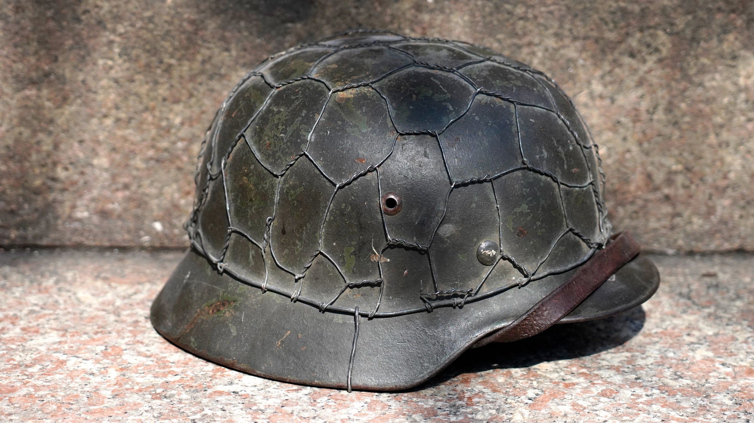 A vintage military helmet covered with protective wire mesh.