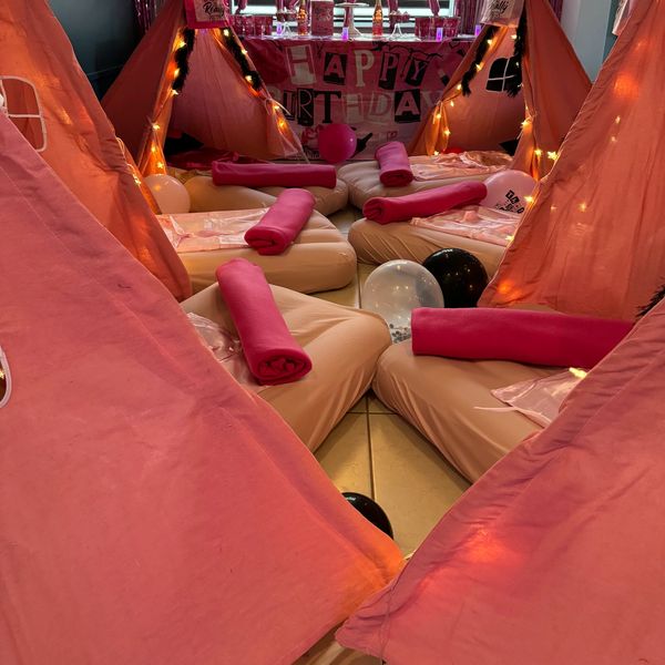 Cozy pink teepee tents set up for a birthday party with cushions and rolled blankets.