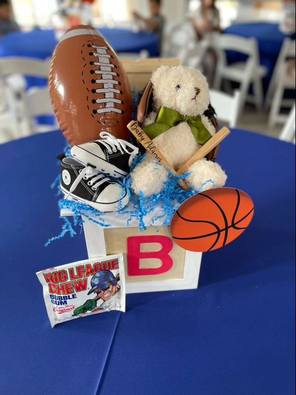 A sports-themed baby gift box with teddy bear, shoes, and toy balls.