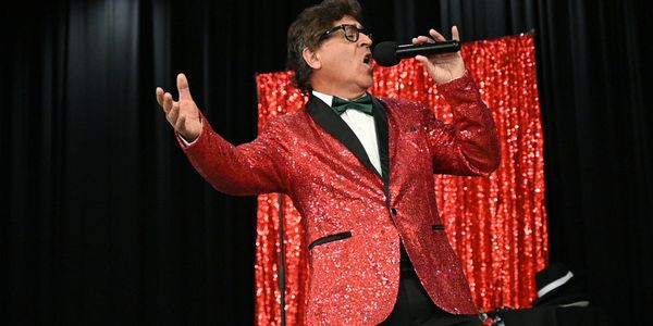 Man passionately singing on stage in a sparkling red jacket.