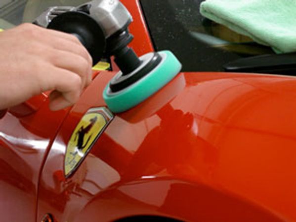 Person polishing a red Ferrari car's exterior with a buffer.