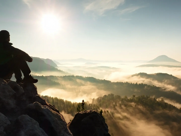 Man and dog sitting on a mountain overlooking a sunrise
