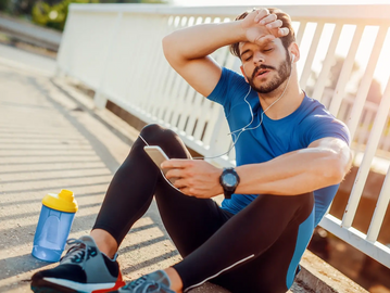 Man post run sweating with hand on head and listing to music through his phone
