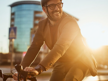 Man on Bike with brown blazer with sun peaking over his shoulder smiling