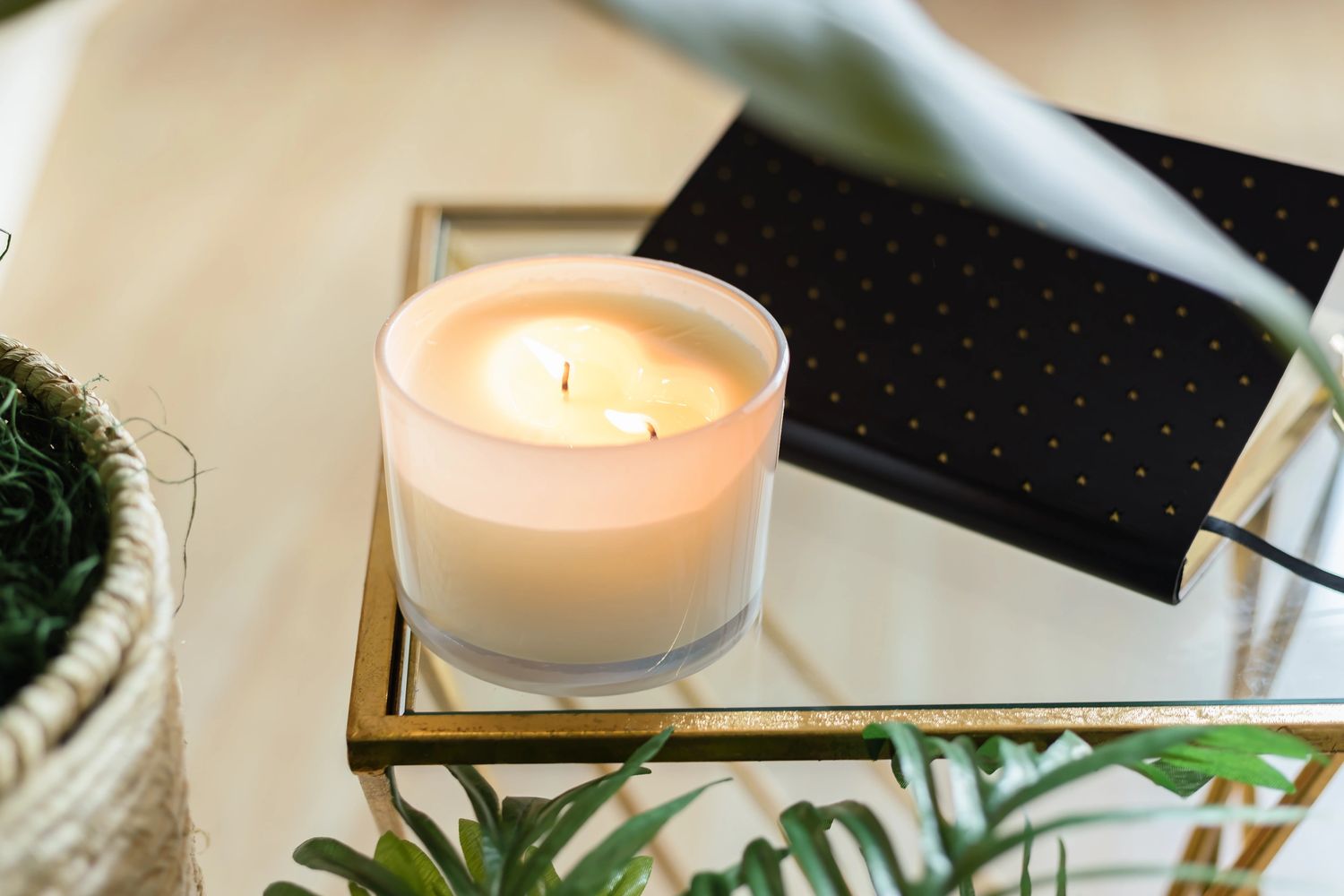 A lit candle in a frosted glass holder on a mirrored tray with green plants.