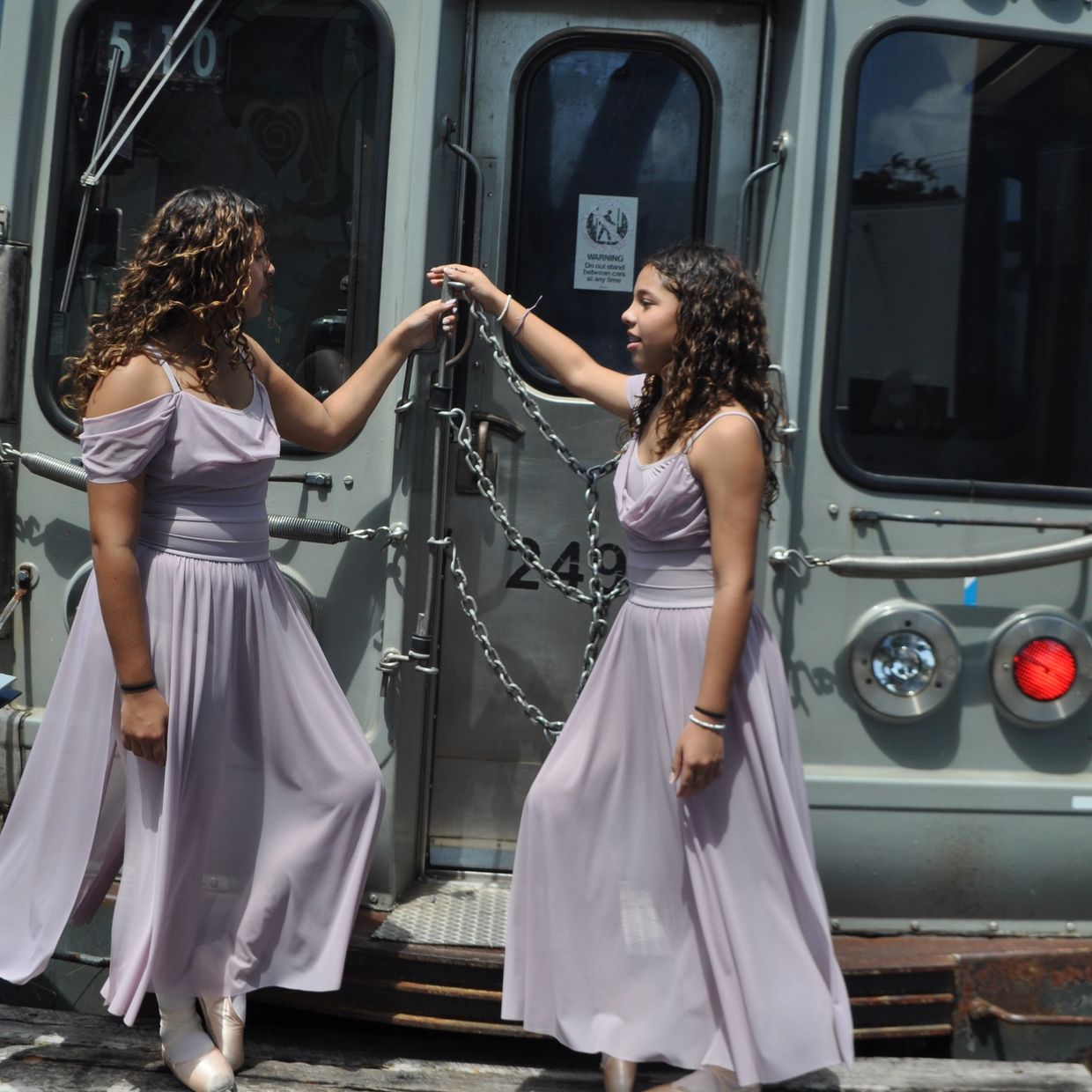 Two girls in lavender dresses holding hands near a vintage trolley door.