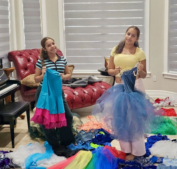 Two women holding colorful dresses in a room filled with fabric.