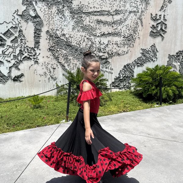 Young girl twirling in a red and black flamenco dress outdoors.