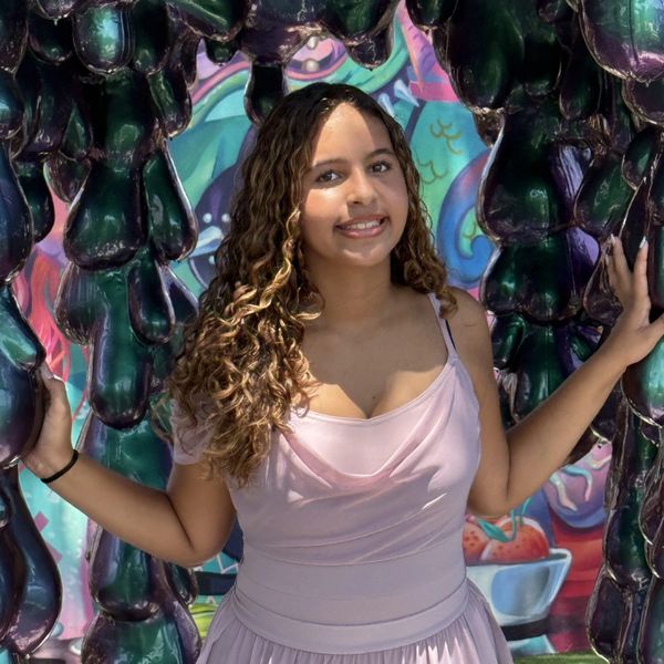 Young woman in a pink dress posing with abstract dark green sculpture.