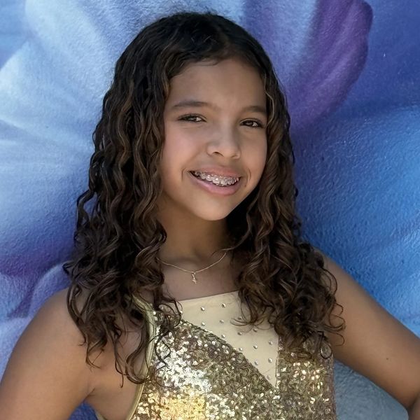 Smiling girl with curly hair and braces in a gold sequined dress.
