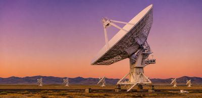 Large satellite dishes in a desert landscape during sunset.
