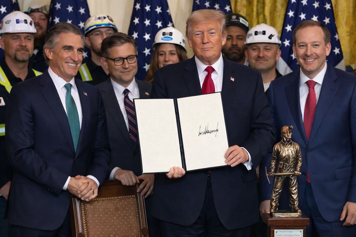 Former President Trump holds signed document surrounded by officials and workers in hard hats.