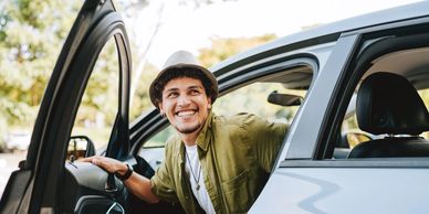Joven sonriendo junto a su carro, disfrutando de la 
 tranquilidad de contar con un seguro de autos