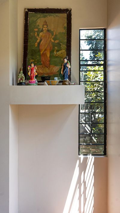A serene prayer corner with Hindu deity statues and a framed painting near a sunlit window.