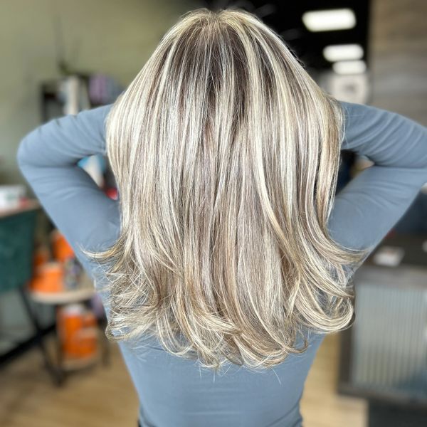 Blonde layered haircut with highlights, styled straight and curled at the ends.