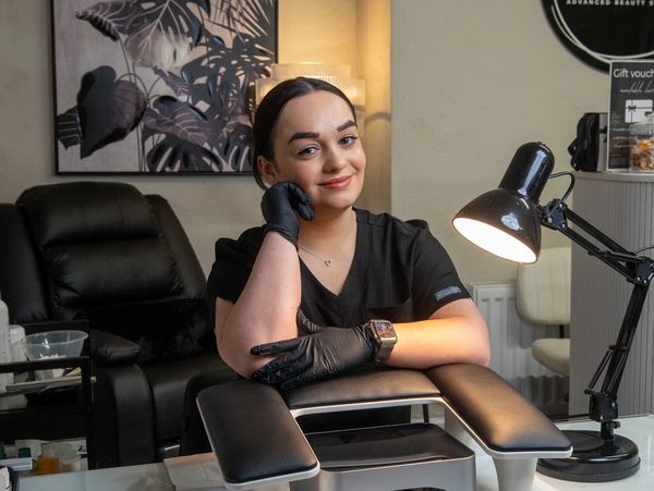 A smiling woman in black gloves sitting at a manicure station.