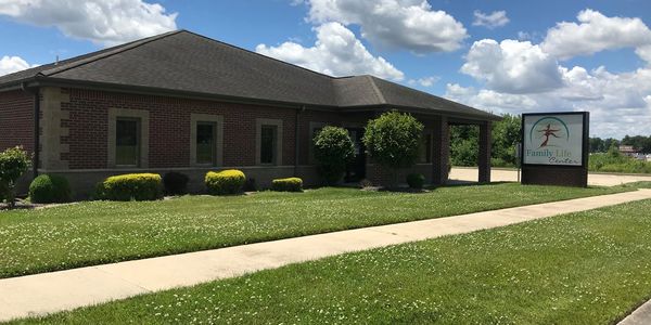 Brick building with shrubs and a Family Life Center sign under a blue sky.