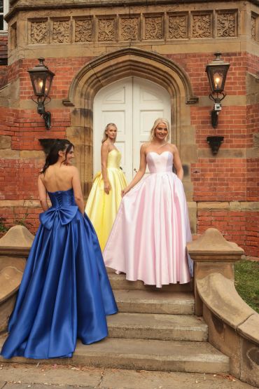 Three women in colorful ball gowns outside a grand entrance.