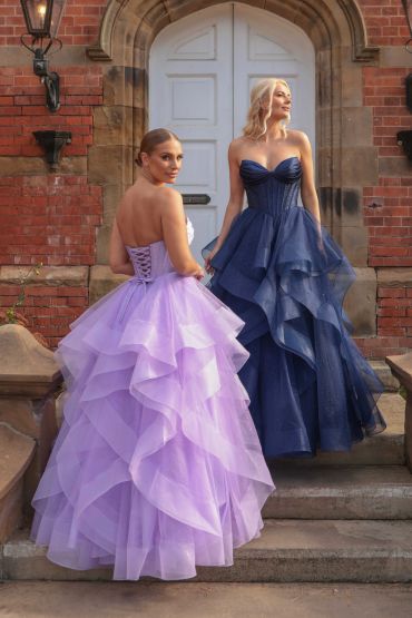 Two women wearing layered ball gowns in front of a grand door.
