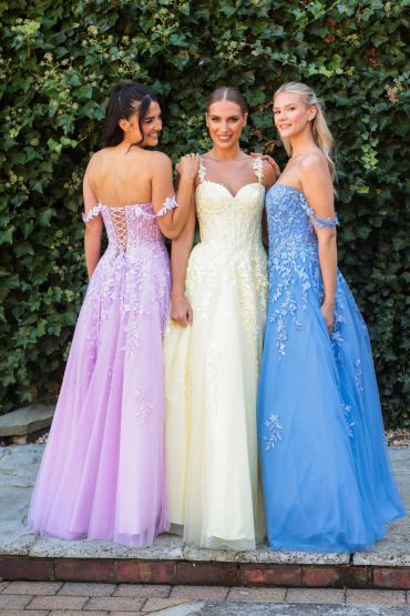 Three women in elegant pastel gowns posing outdoors.