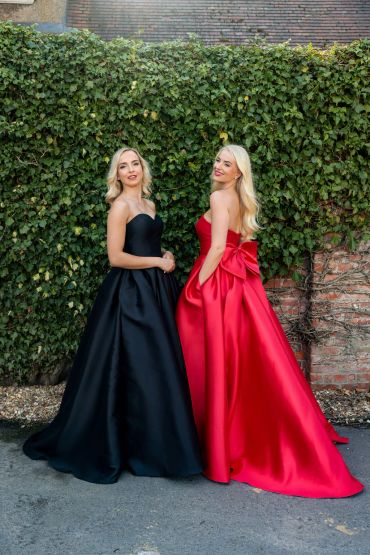 Two women in elegant black and red gowns posing outdoors.