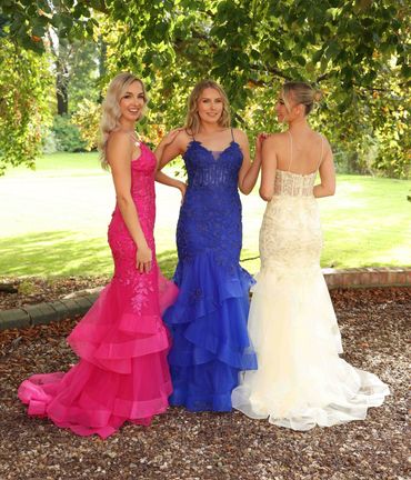 Three women in elegant colorful gowns outdoors.