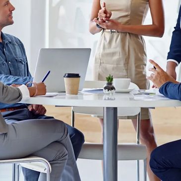 A group of professionals engaged in a business meeting around a table with laptops and coffee.