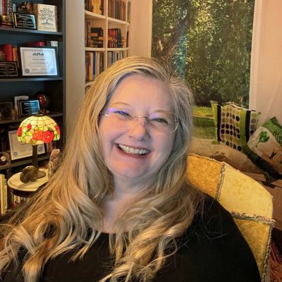 Smiling woman with long blonde hair in a cozy room.