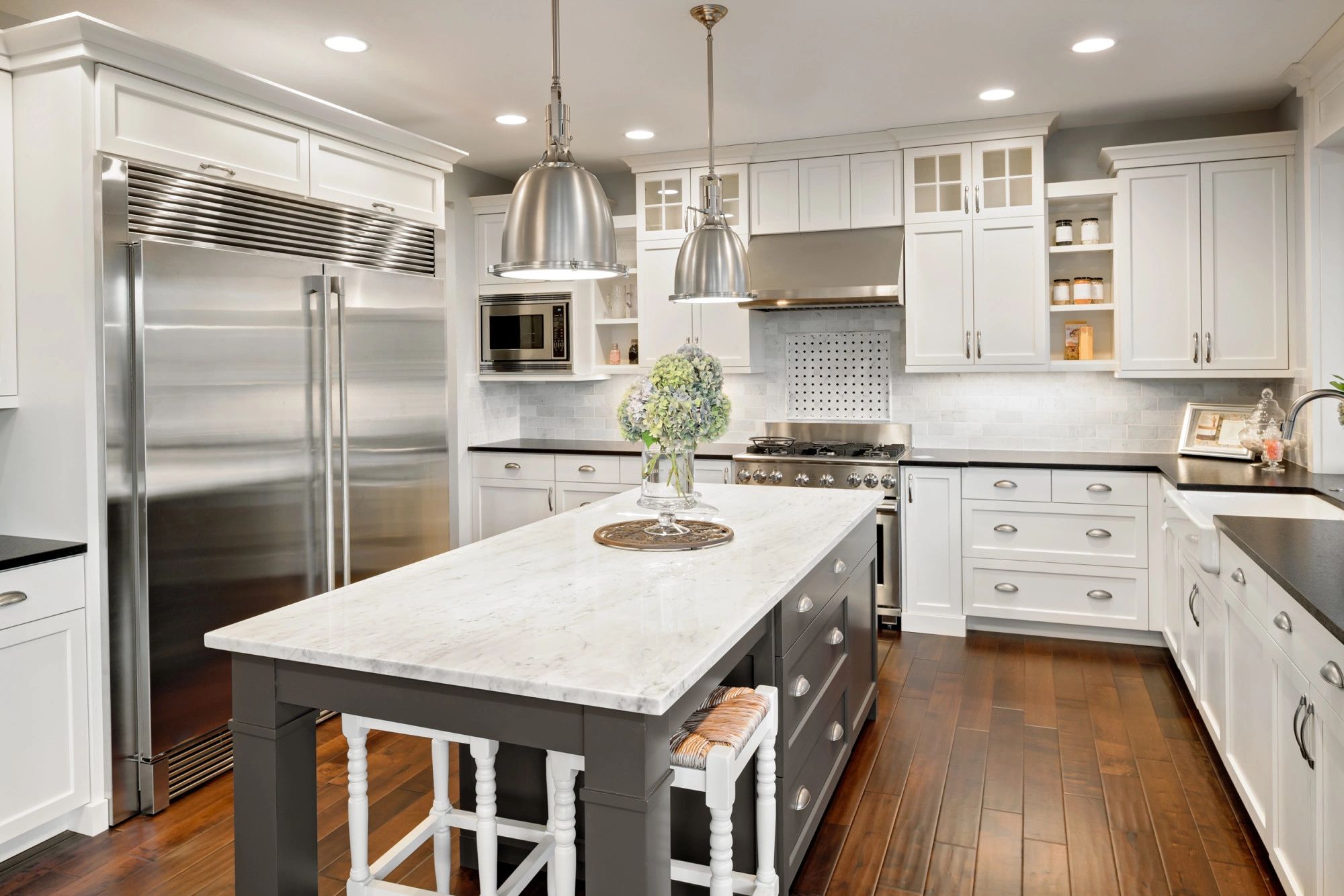 Modern kitchen with white cabinets, stainless steel appliances, and a marble island.