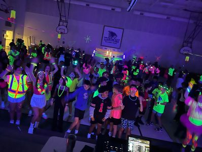 Students enjoying a glow party in a school gym with neon and blacklight decor.