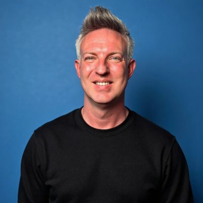 Man with gray hair smiling against a blue background.