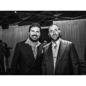 Two men in suits posing and smiling at an indoor event.