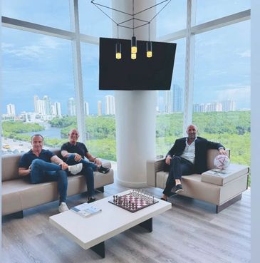 Three men sitting in a modern lounge with a chessboard and city view.