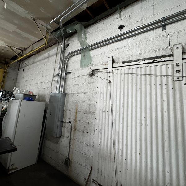 Industrial wall with electrical conduits and a metal sliding door in a dimly lit Commercial kitchen warehouse.