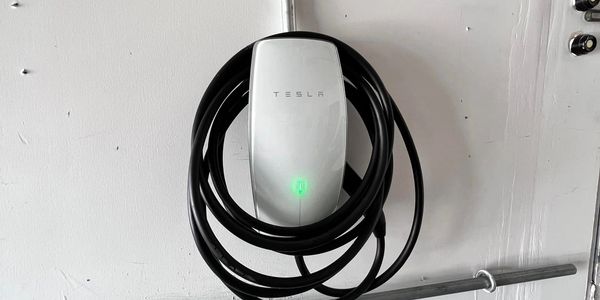 Tesla electric vehicle charger mounted on a wall with coiled cable.