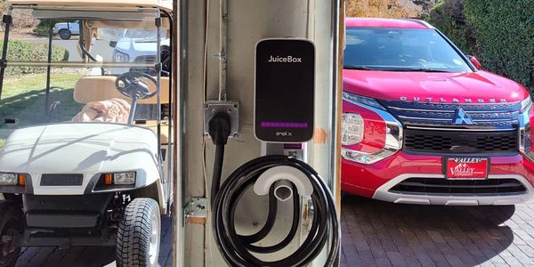 Electric car charger mounted between a golf cart and a red Mitsubishi Outlander.