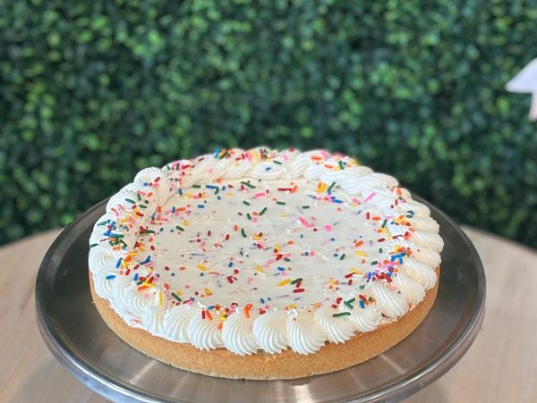 A round cake with white frosting and colorful sprinkles.