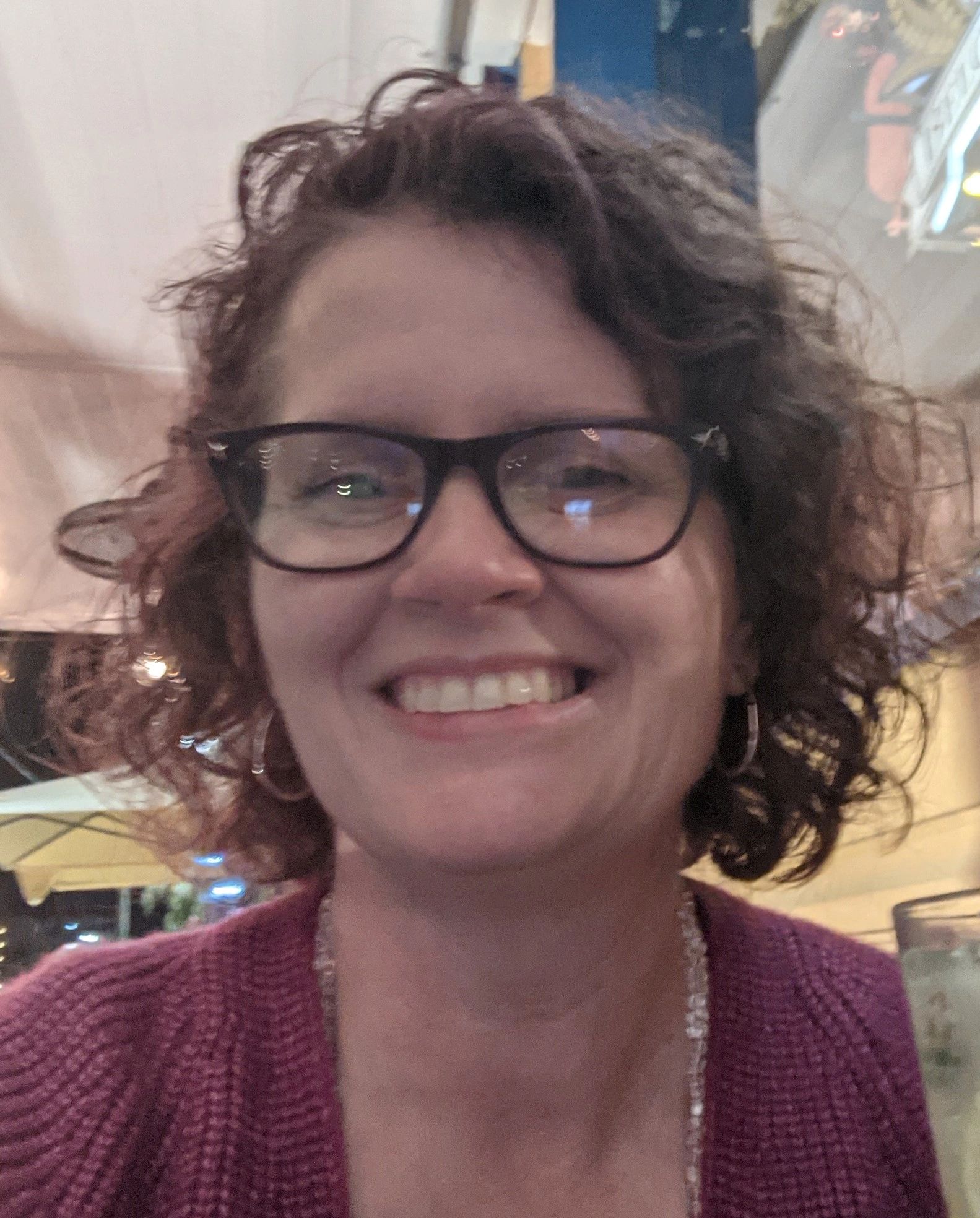 Picture head shoulder close-up of owner of the site. Short curly brunette hair with pink sweater and