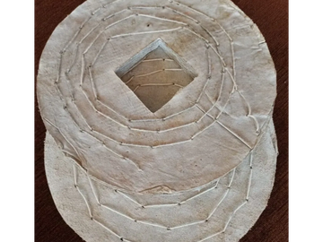 Two circular, stitched leather pieces with geometric patterns, one featuring a diamond-shaped cutout.