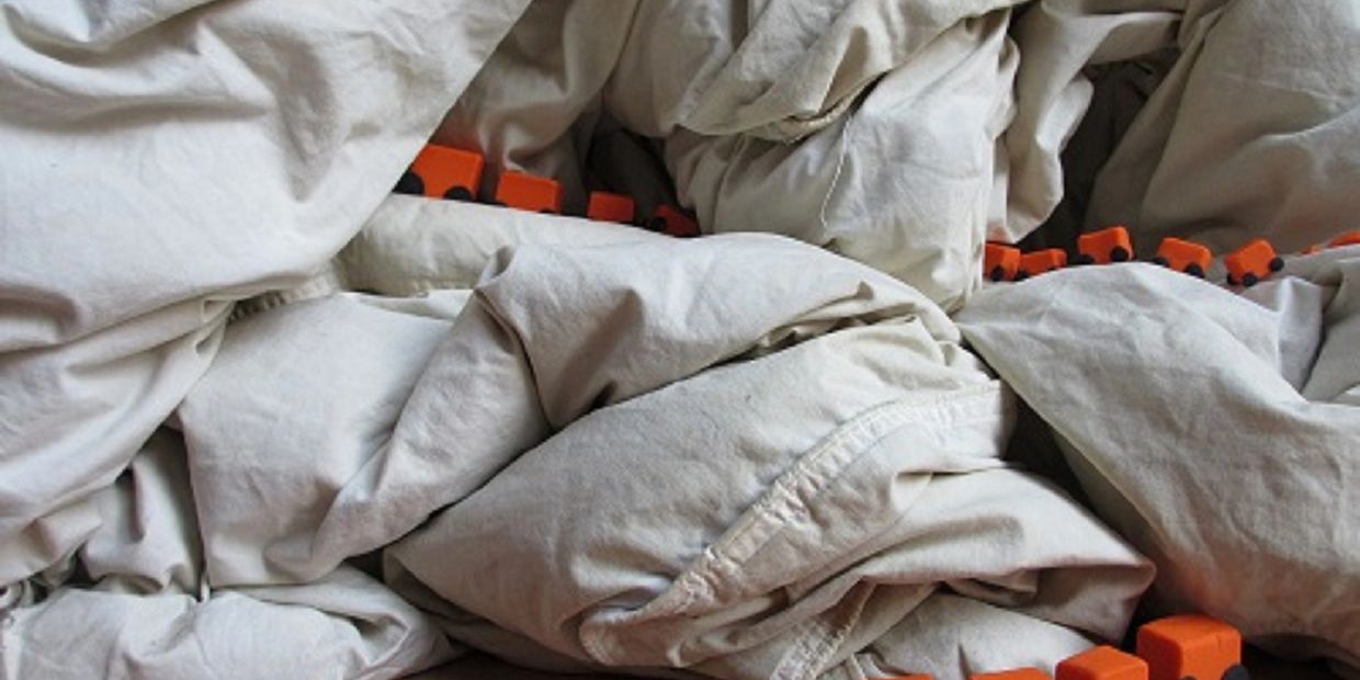 Orange train hidden under beige blanket folds.