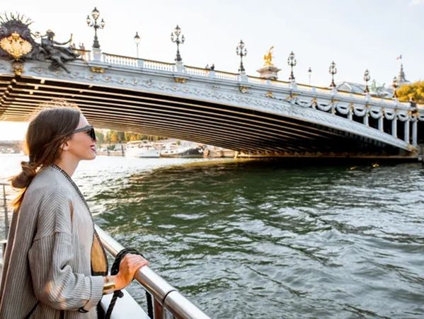Woman enjoying a scenic river view near an ornate bridge.