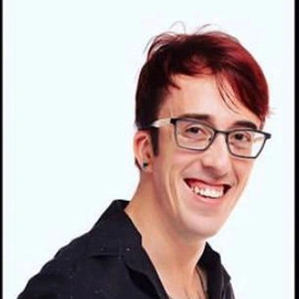 Smiling young man with glasses and tattoos wearing a black shirt.